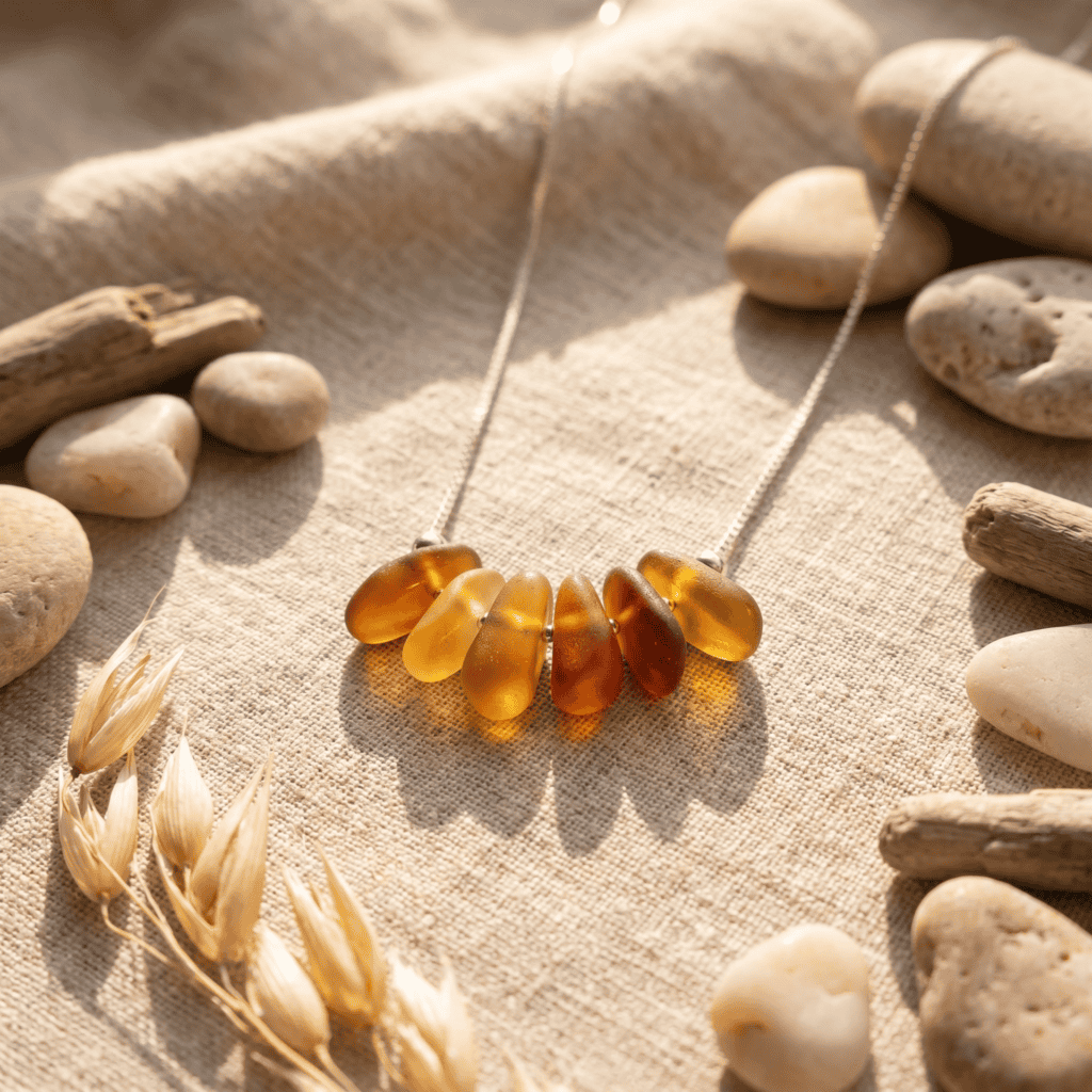 Amber sea glass necklace displayed on beige fabric with stones and driftwood.