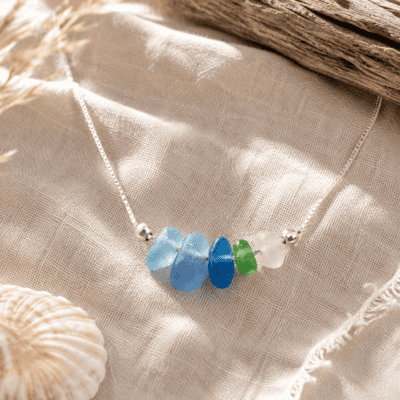 Sea glass necklace with blue, green, and white beads on beige fabric.
